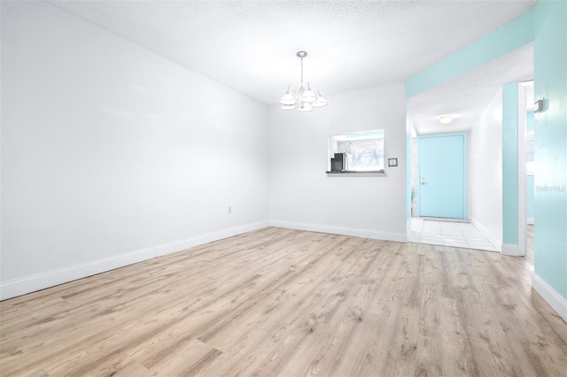 unfurnished room featuring light hardwood / wood-style flooring, a textured ceiling, and a notable chandelier