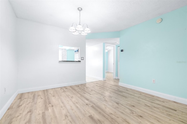 spare room with light hardwood / wood-style flooring, a textured ceiling, and an inviting chandelier