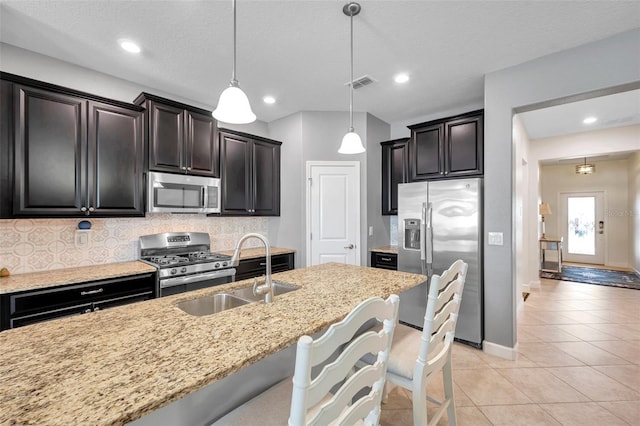 kitchen with a kitchen bar, backsplash, light stone counters, stainless steel appliances, and decorative light fixtures