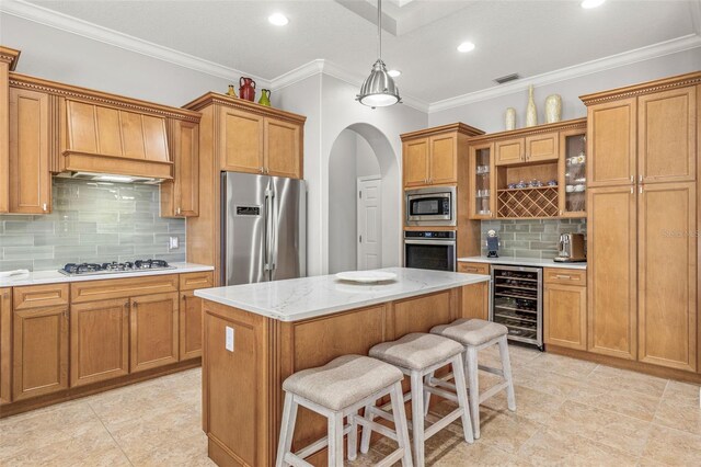 kitchen featuring ornamental molding, stainless steel appliances, beverage cooler, a center island, and a breakfast bar area