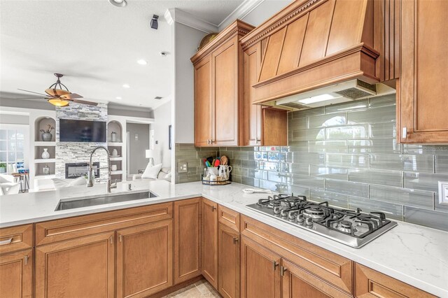 kitchen with backsplash, custom range hood, stainless steel gas cooktop, sink, and a fireplace