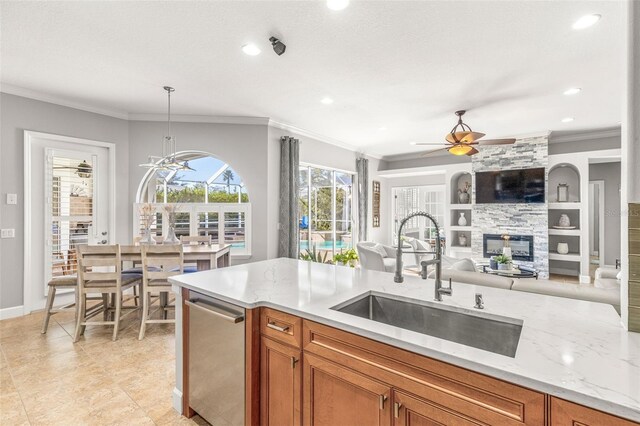 kitchen with ceiling fan with notable chandelier, crown molding, sink, decorative light fixtures, and a stone fireplace