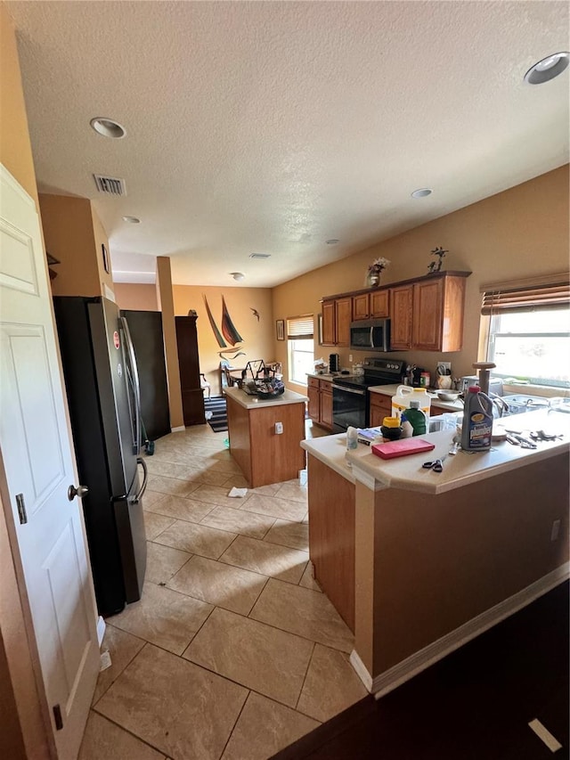 13404 Hampton Park Ct, Fort Myers, FL 33913 - kitchen featuring stainless steel appliances, brown cabinets, a center island, healthy amount of natural light, and a textured ceiling