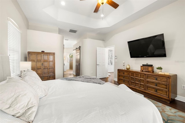 bedroom featuring hardwood / wood-style floors, ceiling fan, a barn door, and a tray ceiling