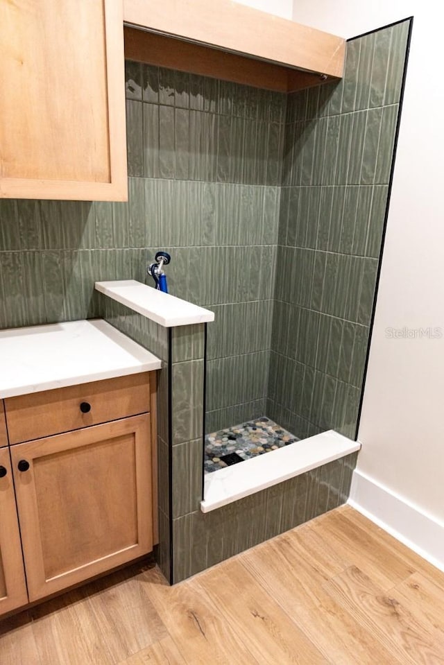 bathroom with hardwood / wood-style floors, tiled shower, and tile walls