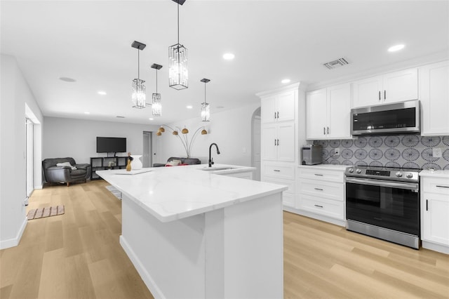 kitchen featuring appliances with stainless steel finishes, a center island with sink, white cabinetry, and light hardwood / wood-style flooring