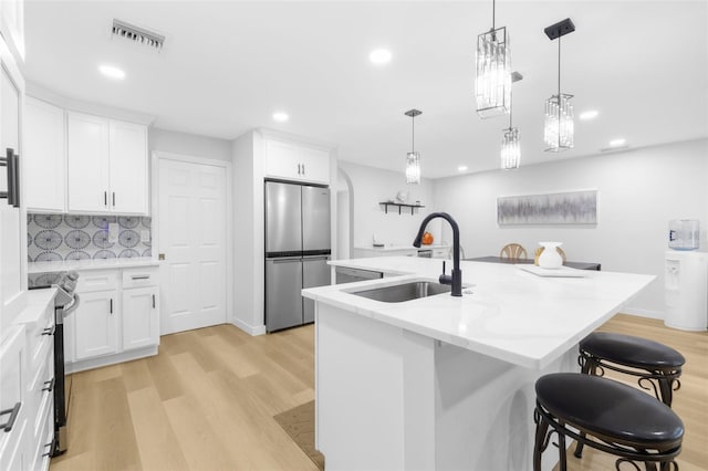 kitchen with a kitchen island with sink, white cabinets, decorative backsplash, light wood-type flooring, and stainless steel appliances