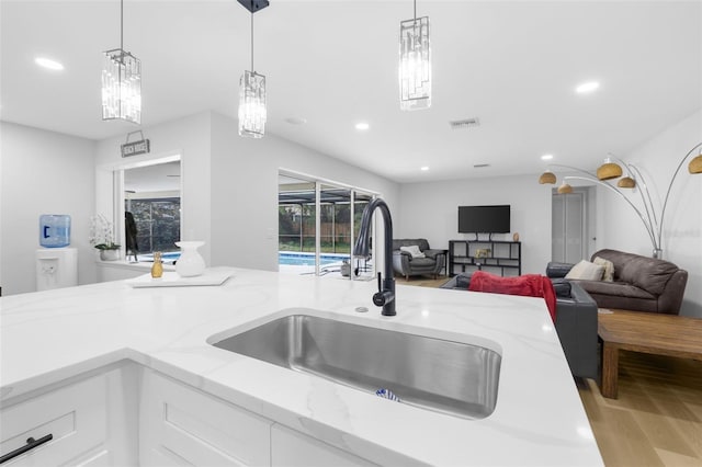 kitchen featuring white cabinetry, light stone countertops, sink, light hardwood / wood-style flooring, and pendant lighting