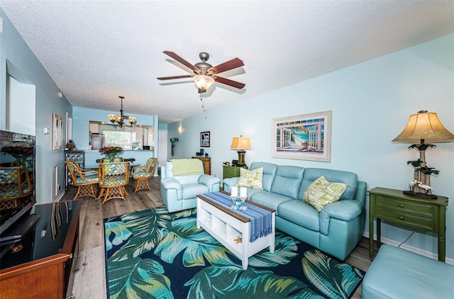 living room with ceiling fan with notable chandelier, wood-type flooring, and a textured ceiling