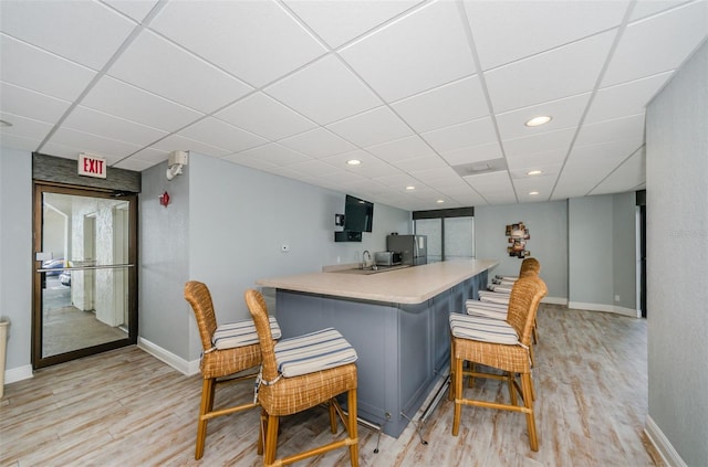 bar featuring a paneled ceiling, stainless steel fridge, and light hardwood / wood-style flooring