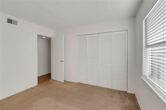 unfurnished bedroom featuring light colored carpet, a textured ceiling, and a closet