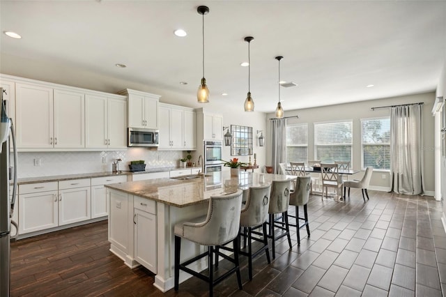 kitchen featuring appliances with stainless steel finishes, a kitchen island with sink, sink, pendant lighting, and white cabinetry