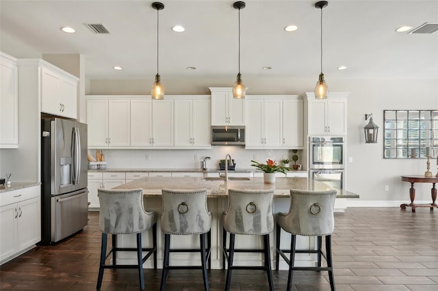 kitchen with pendant lighting, stainless steel appliances, and a center island with sink