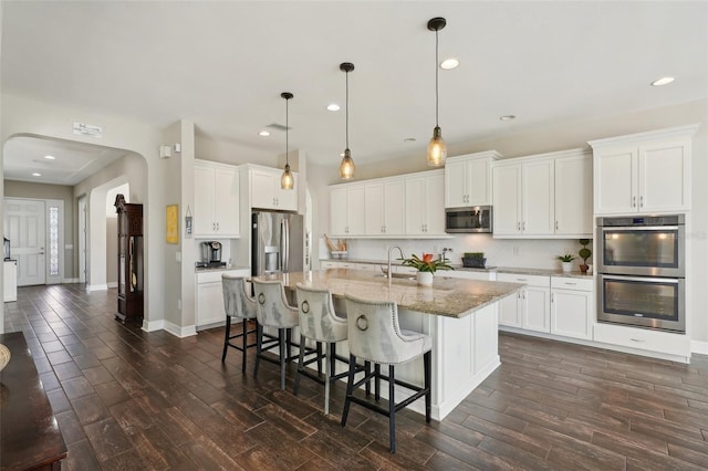 kitchen featuring white cabinets, decorative light fixtures, a center island with sink, and appliances with stainless steel finishes