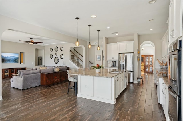 kitchen with stainless steel appliances, a kitchen island with sink, dark wood-type flooring, white cabinetry, and hanging light fixtures