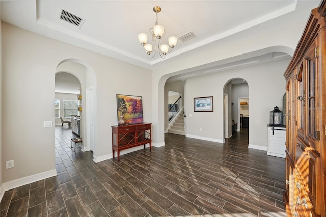 interior space with a raised ceiling, dark hardwood / wood-style floors, and a notable chandelier