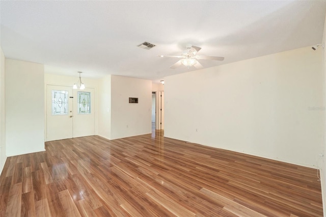 empty room with ceiling fan with notable chandelier and hardwood / wood-style flooring