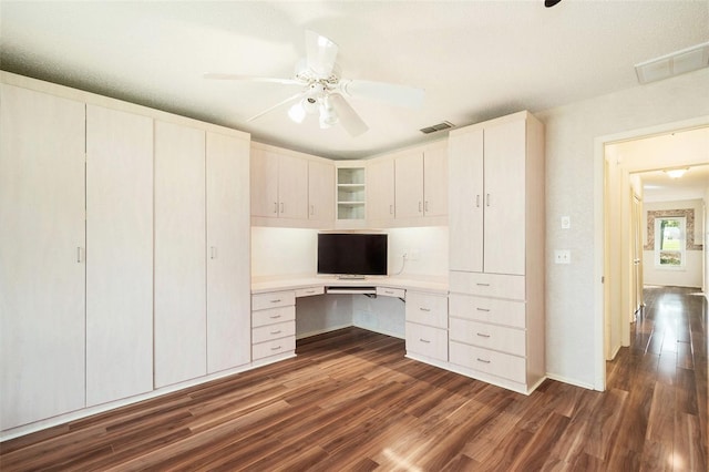 unfurnished office featuring a textured ceiling, ceiling fan, built in desk, and dark hardwood / wood-style floors