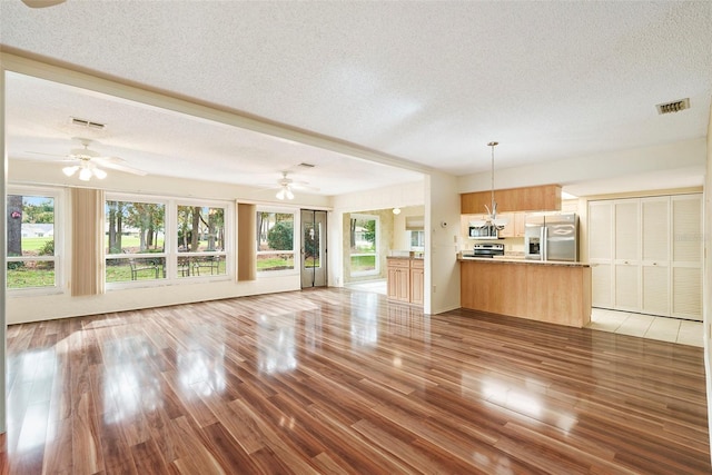 unfurnished living room with ceiling fan, light hardwood / wood-style floors, and a textured ceiling