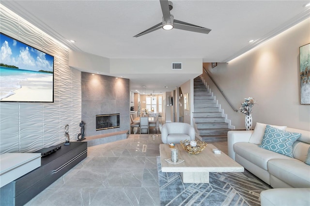 living room featuring ceiling fan, ornamental molding, and a tile fireplace