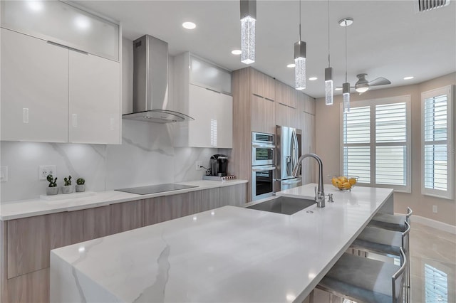 kitchen featuring a kitchen breakfast bar, stainless steel appliances, wall chimney range hood, decorative light fixtures, and a center island with sink