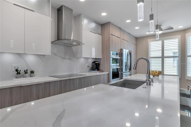 kitchen featuring wall chimney exhaust hood, light stone counters, stainless steel appliances, and decorative light fixtures