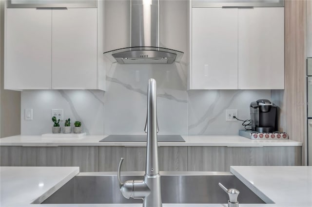 kitchen with light stone countertops, backsplash, white cabinetry, and wall chimney range hood