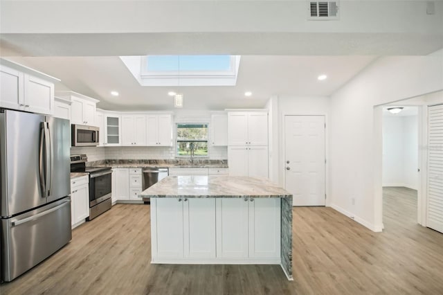 kitchen featuring a kitchen island, light stone counters, white cabinetry, and stainless steel appliances