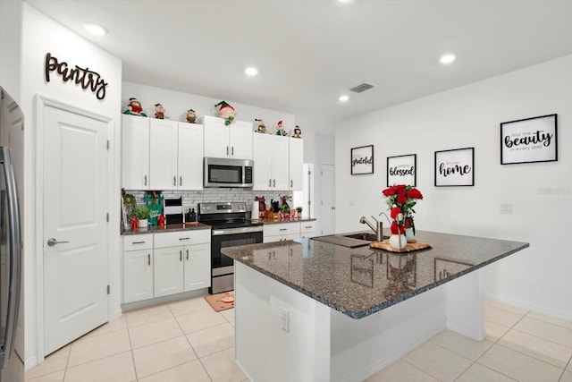 kitchen with stainless steel appliances, white cabinets, dark stone countertops, and tasteful backsplash