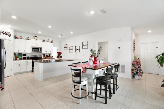 kitchen featuring a center island, stainless steel appliances, dark countertops, light tile patterned flooring, and white cabinetry