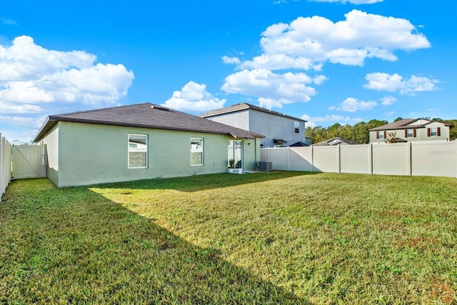 rear view of house with a fenced backyard, a lawn, and stucco siding