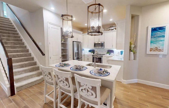 kitchen featuring stainless steel appliances, sink, light hardwood / wood-style flooring, white cabinets, and hanging light fixtures