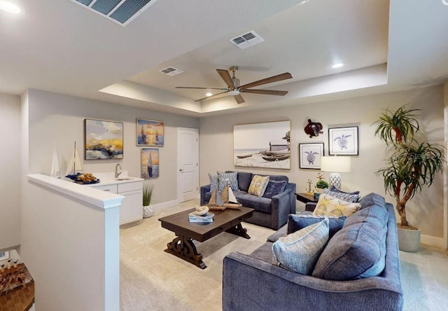 living room with light colored carpet, a raised ceiling, ceiling fan, and sink