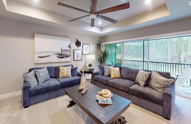 living room with ceiling fan, a raised ceiling, and light carpet