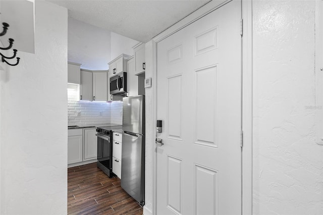 kitchen with appliances with stainless steel finishes, backsplash, a textured ceiling, dark hardwood / wood-style floors, and white cabinetry