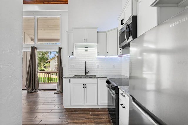 kitchen featuring appliances with stainless steel finishes, dark wood-type flooring, sink, dark stone countertops, and white cabinetry