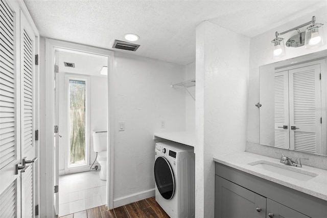 clothes washing area with a textured ceiling, washer / clothes dryer, sink, and dark hardwood / wood-style flooring