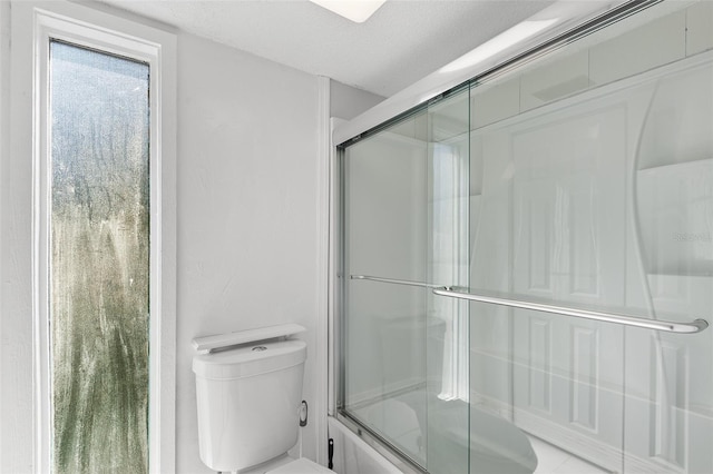 bathroom with a textured ceiling, toilet, and enclosed tub / shower combo