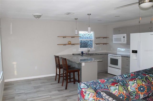 kitchen with gray cabinetry, sink, kitchen peninsula, white appliances, and a kitchen bar