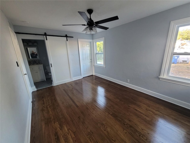 unfurnished bedroom with a barn door, ceiling fan, dark wood-type flooring, and multiple windows