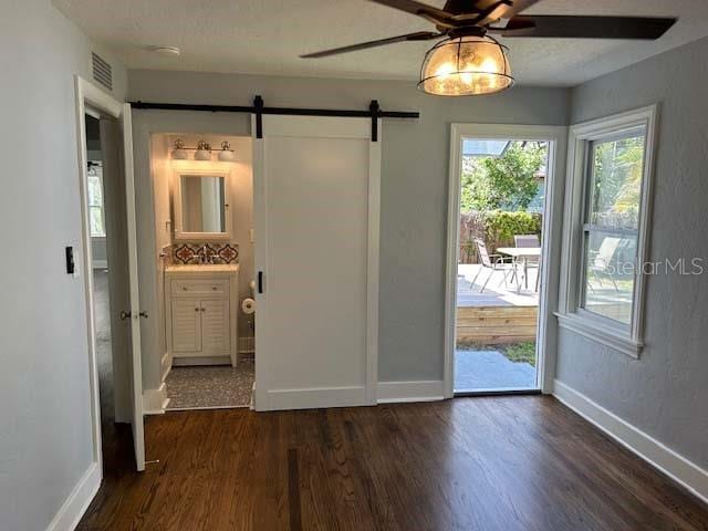 interior space with ceiling fan, a barn door, and dark wood-type flooring