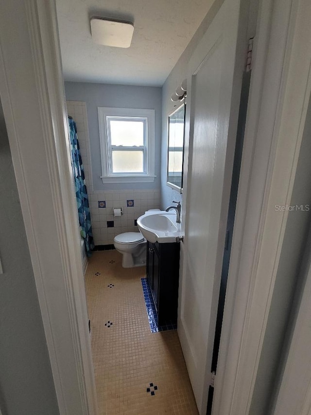 bathroom featuring vanity, tile patterned flooring, toilet, tile walls, and walk in shower