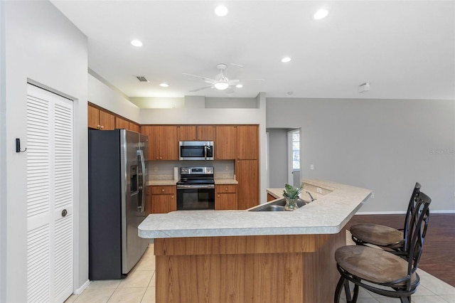 kitchen with ceiling fan, sink, stainless steel appliances, a breakfast bar area, and light tile patterned floors