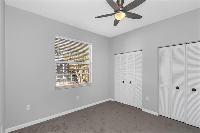 unfurnished bedroom featuring multiple closets, ceiling fan, and dark colored carpet