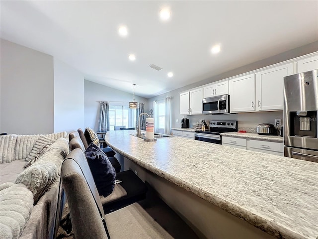 kitchen featuring white cabinets, vaulted ceiling, decorative light fixtures, a kitchen bar, and stainless steel appliances