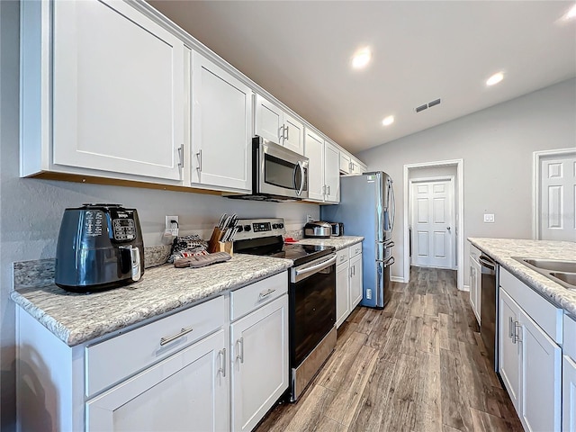 kitchen with light stone countertops, light wood-type flooring, stainless steel appliances, white cabinets, and lofted ceiling