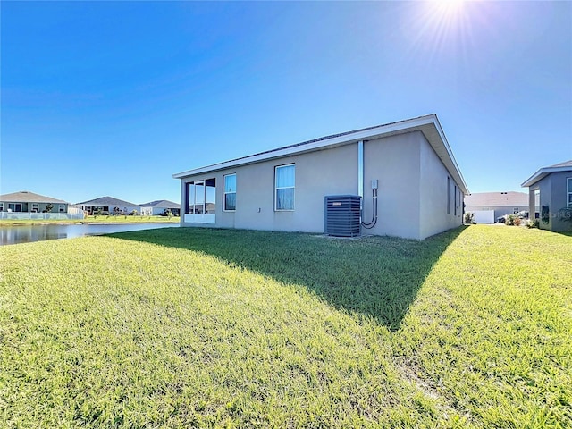 rear view of property with central AC unit, a water view, and a lawn