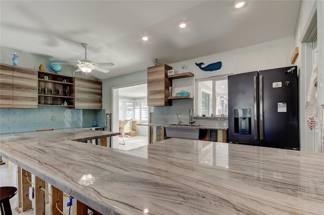 kitchen featuring plenty of natural light, ceiling fan, decorative backsplash, and black refrigerator with ice dispenser