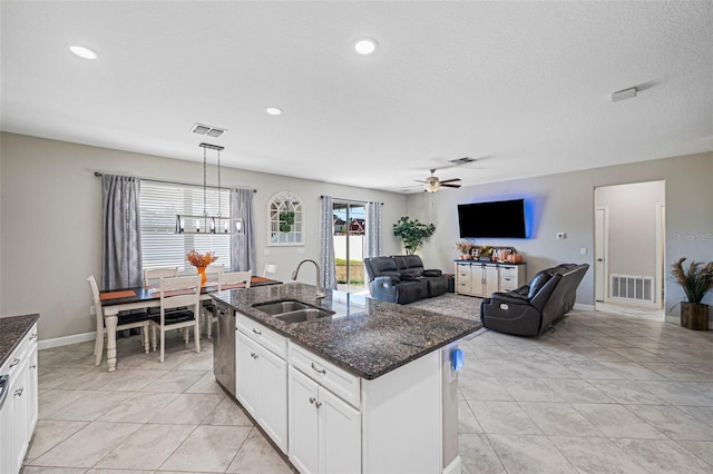 kitchen with dark stone counters, sink, white cabinets, hanging light fixtures, and an island with sink