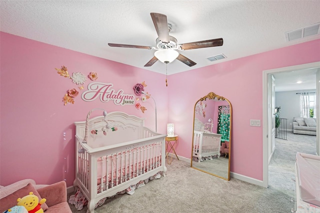 bedroom featuring carpet flooring, ceiling fan, a textured ceiling, and a crib